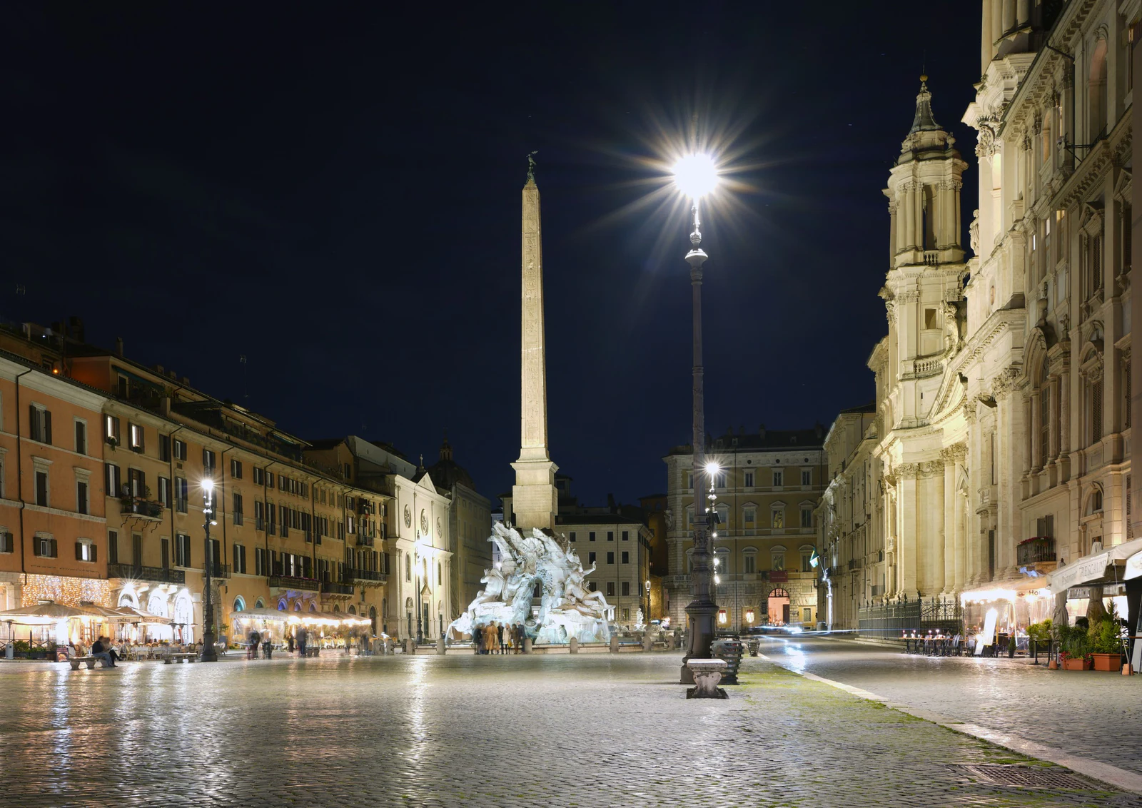 A praça já completamente noturna, com a Fontana dei Quattro Fiumi e o obelisco dominando o centro. É uma imagem diferent