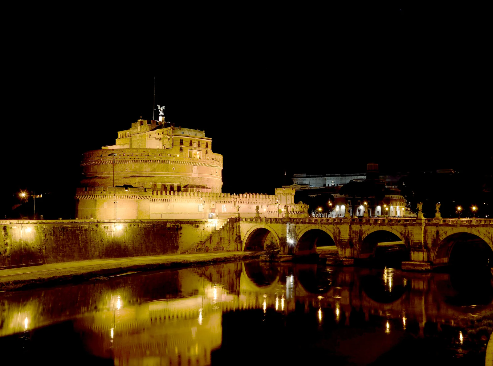 Vista mais aberta à noite, com Ponte Sant&rsquo;Angelo e os reflexos no Tibre. É a imagem que melhor mostra por que a região t
