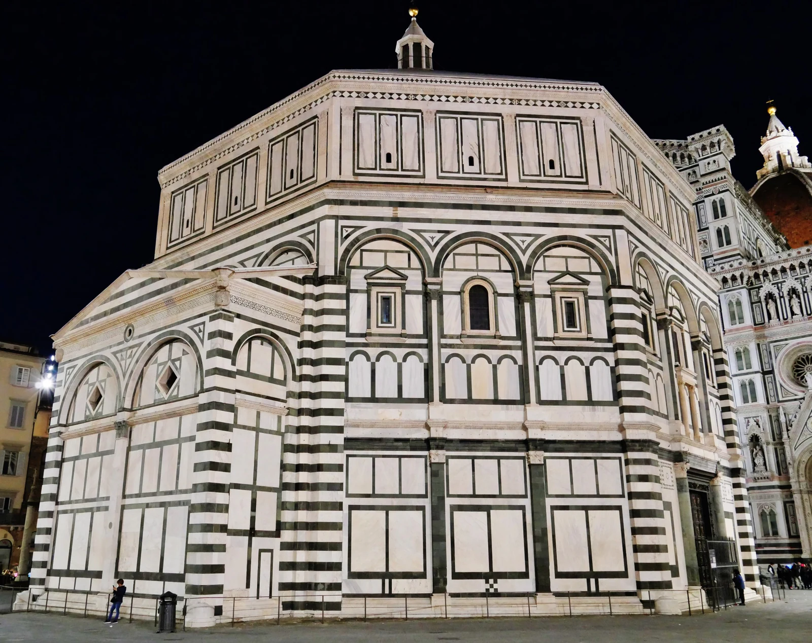 O Batistério à noite, com o Duomo aparecendo ao fundo. É uma ótima imagem para guardar porque o revestimento preto e bra