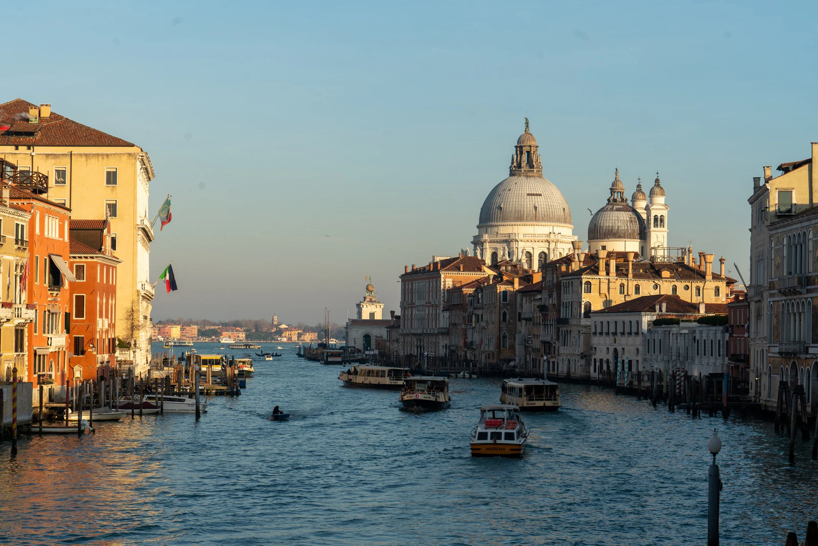 Canal Grande em luz dourada, com Santa Maria della Salute ao fundo e barcos cruzando a água. É a imagem mais cinematográ