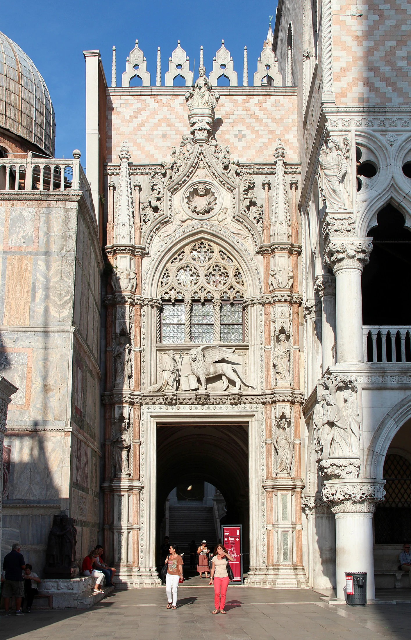 A Porta della Carta, passagem cerimonial entre o palácio e San Marco. Sobre a porta, o doge Francesco Foscari aparece ajoelhado diante do leão de São Marcos: a imagem resume a ideia central da República — o governante existe abaixo do santo, do Estado e de suas instituições, não acima deles.