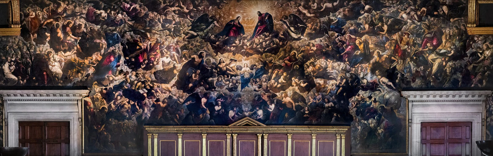 O Paradiso de Jacopo e Domenico Tintoretto ocupando a parede atrás do trono do doge. A multidão de figuras é quase impossível de ler de uma vez — e esse excesso é deliberado: depois do incêndio de 1577, Veneza reconstruiu a sala e substituiu a perda por uma afirmação ainda maior de continuidade, ordem celestial e poder político.