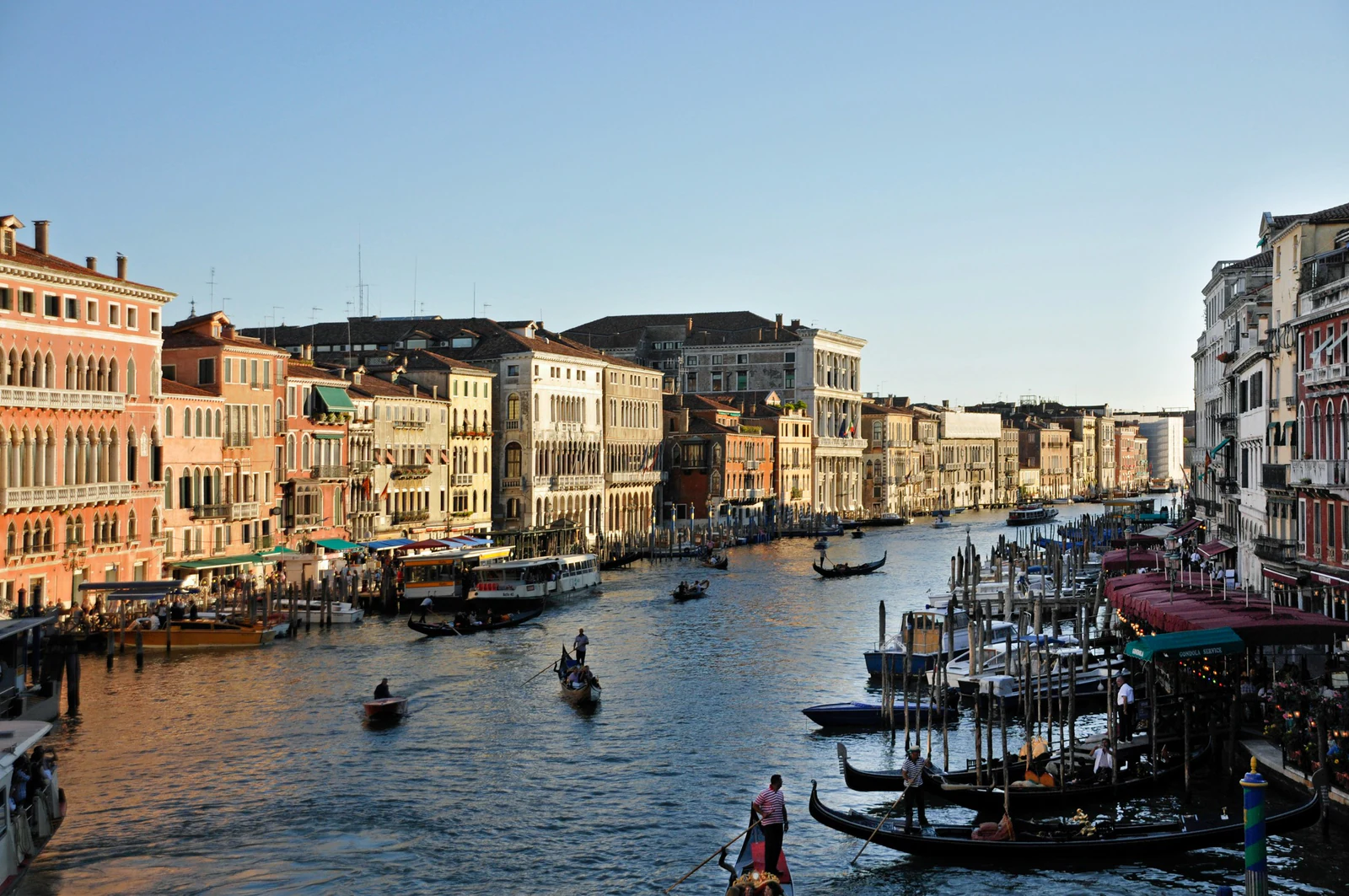 A recompensa da passagem externa é esta leitura longitudinal do Canal Grande. Em vez de procurar apenas uma selfie, acompanhe palácios, fachadas de armazéns, pontili e embarcações: o panorama explica como água, representação social e logística mercantil ocupavam o mesmo eixo urbano.