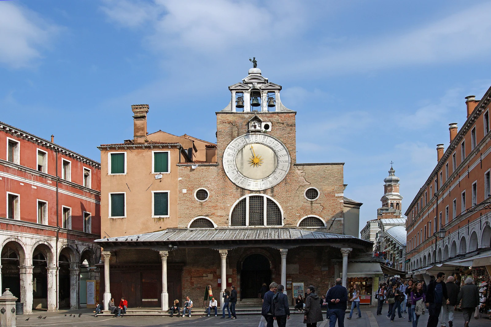 San Giacomo di Rialto — San Giacometo para os venezianos — organiza o campo com seu pórtico e o enorme mostrador de 24 horas. A tradição local empurra a fundação até 421, mas o edifício atravessou reconstruções e restaurações; o ponto mais seguro é lê-lo como a igreja histórica dos mercadores.