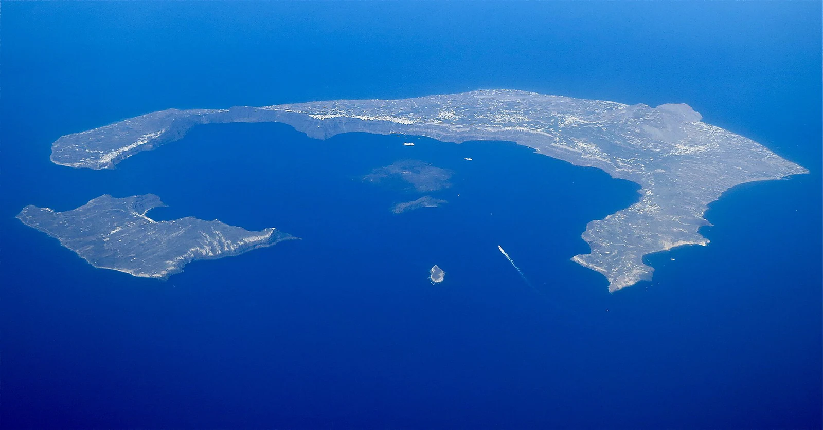 A vista aérea torna a caldeira inteligível de uma vez: Thera forma a grande meia-lua, Therasia fecha o lado oeste e Nea/Palea Kameni ocupam o centro.